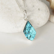 Teardrop-shaped turquoise pendant on a silver chain against a stone background